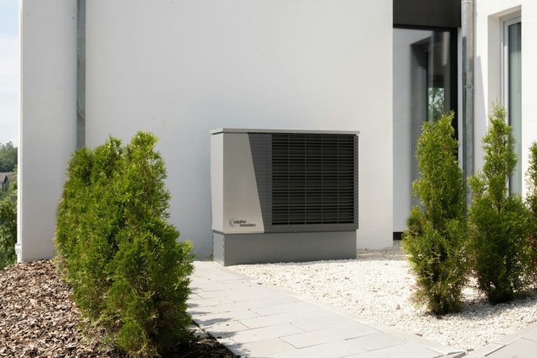 Energieeffiziente Wärmepumpe neben einer modernen Gebäudefassade, umgeben von Pflanzen.
