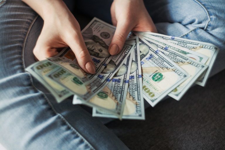 Eine Person hält mehrere 100-Dollar-Scheine in den Händen.