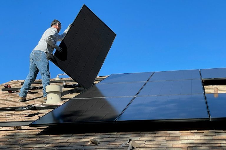 Handwerker montiert ein Solarpanel auf einem Dach unter klarem blauen Himmel.
